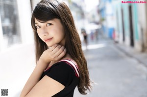 A woman in a black dress leaning against a wall.