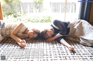 Two young women laying on a bed together. 