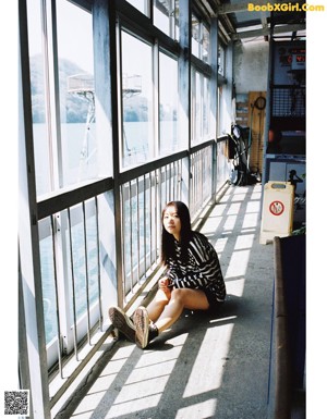 A woman standing in front of a window looking out at the water.
