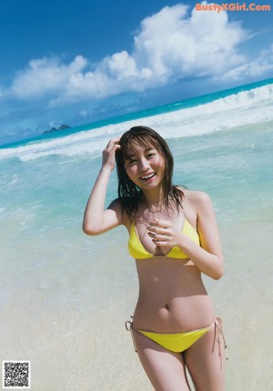 A woman in a yellow bikini sitting on the beach.