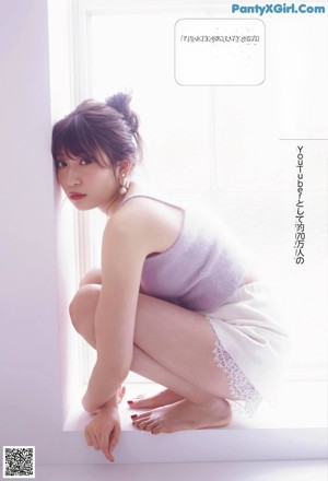 A woman leaning against a wall in a pink top and skirt.