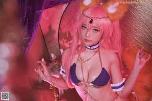 A woman with pink hair wearing a purple and gold outfit.