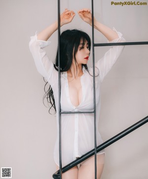 A woman in a white shirt and black skirt is standing in front of a wall of wood slices.