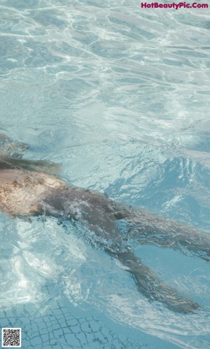 A woman in a bathing suit leaning on the edge of a swimming pool.