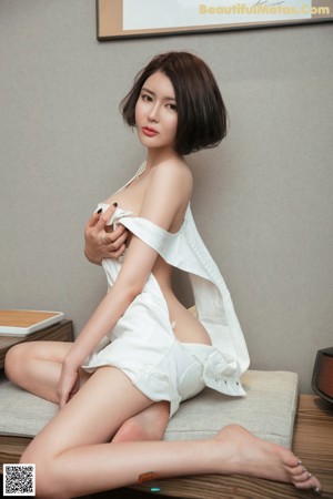 A woman in a white shirt is posing on a bed.